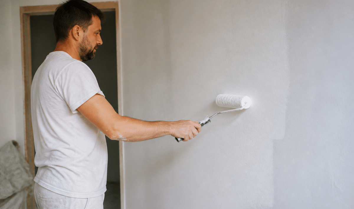 Peintre tenant rouleau appliquant peinture blanche sur mur vertical